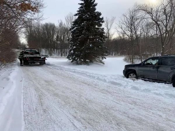 Snowy rural road with parked pickup trucks and a large evergreen tree in the center.