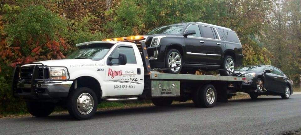 Tow truck hauling two wrecked SUVs on a roadside with trees in the background