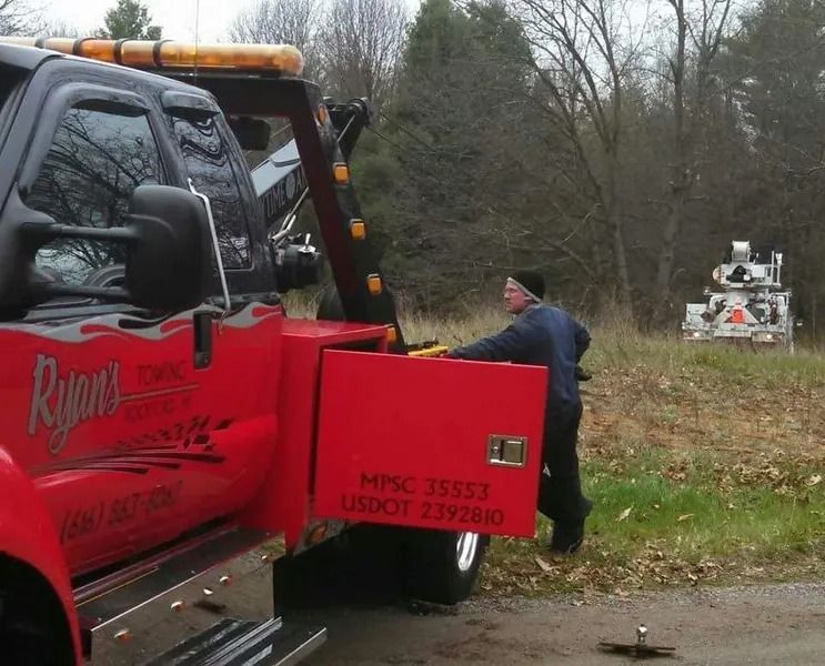 Tow truck worker unloading a red truck on a roadside, with an ambulance in the background