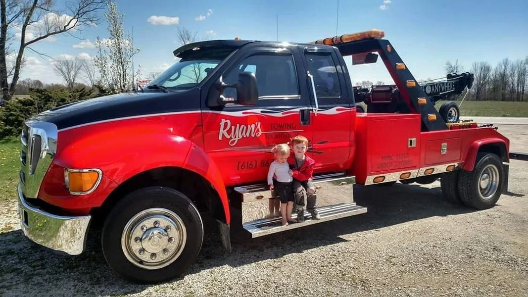 Red tow truck parked outdoors with two children standing on the side step.