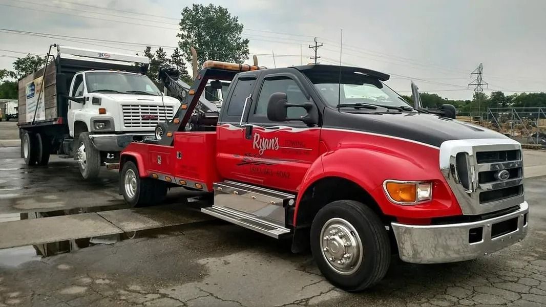 Two tow trucks parked in a wet lot, a red tow truck in front of a white one.