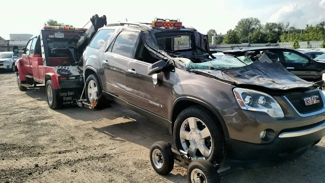 Two SUVs on tow dollies in a gravel lot, one silver and one red, with loaded roof racks.