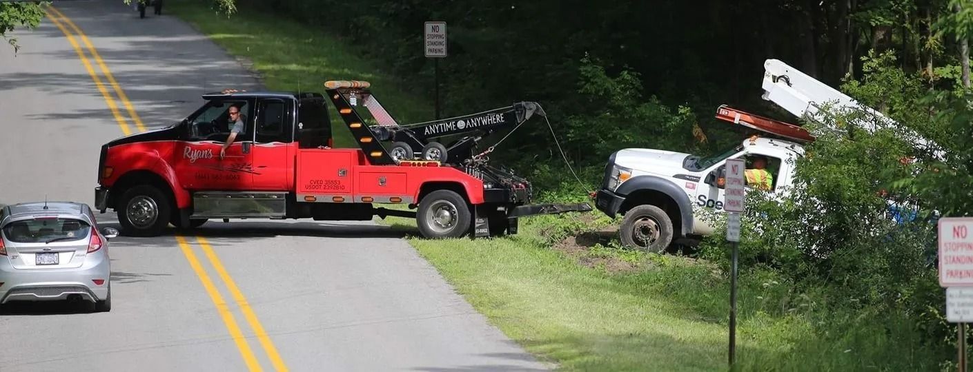 Red and white tow trucks block a road, handling a crash scene on a wooded roadside