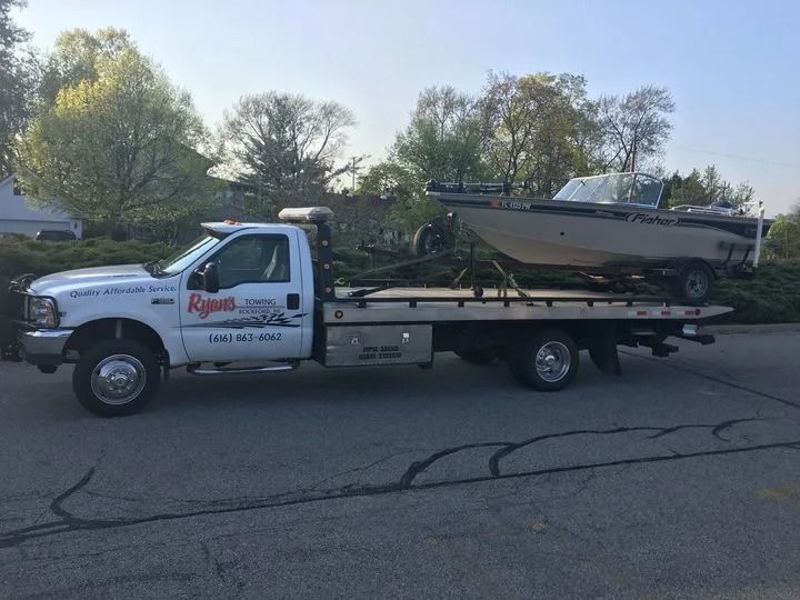 White flatbed tow truck hauling a small boat trailer on a road near trees at dusk