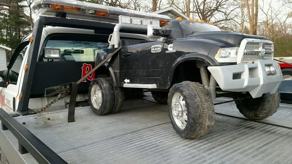 Black toy truck secured on a tow truck bed with a winch strap over the hood