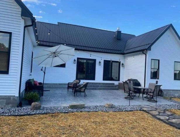 A white house with a black roof and a patio with chairs and umbrellas