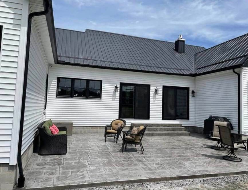 A white house with a black roof and a patio with chairs and a table.