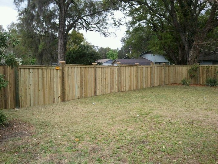 A new wooden privacy fence encloses a grassy backyard, with trees visible behind it.