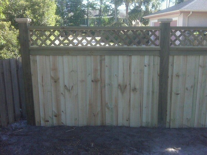New wooden fence with vertical pickets and a top lattice panel between square posts in a residential yard.