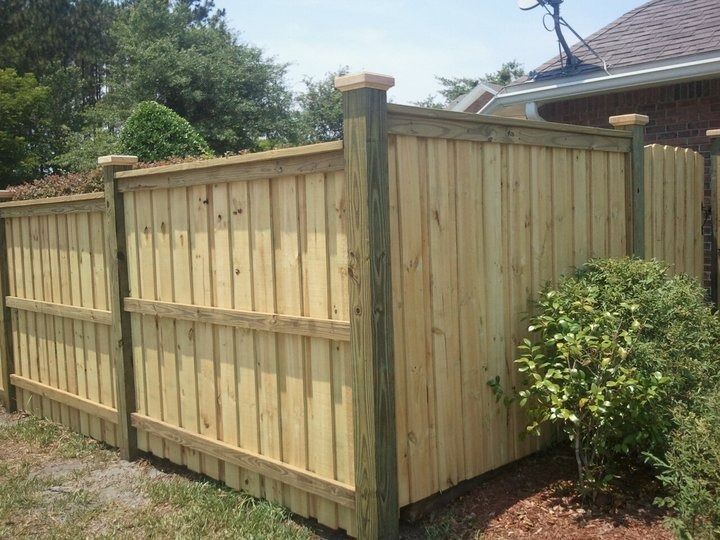 A new wooden privacy fence with vertical panels, horizontal support rails, and square post caps outdoors.