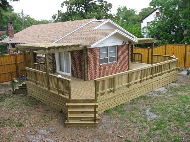 A brick house with a newly built, large wooden deck and a pergola, surrounded by a wood fence in a yard.