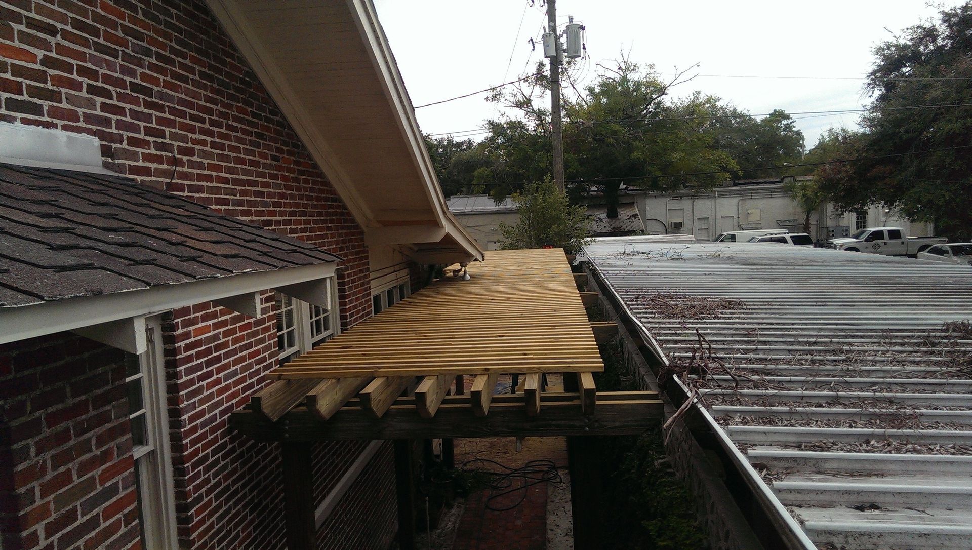 Plywood decking being installed on wooden rafters of a structure attached to a red brick building.