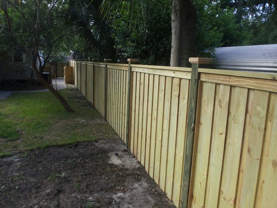 A newly installed wooden privacy fence with vertical panels and capped posts runs along a grassy yard.