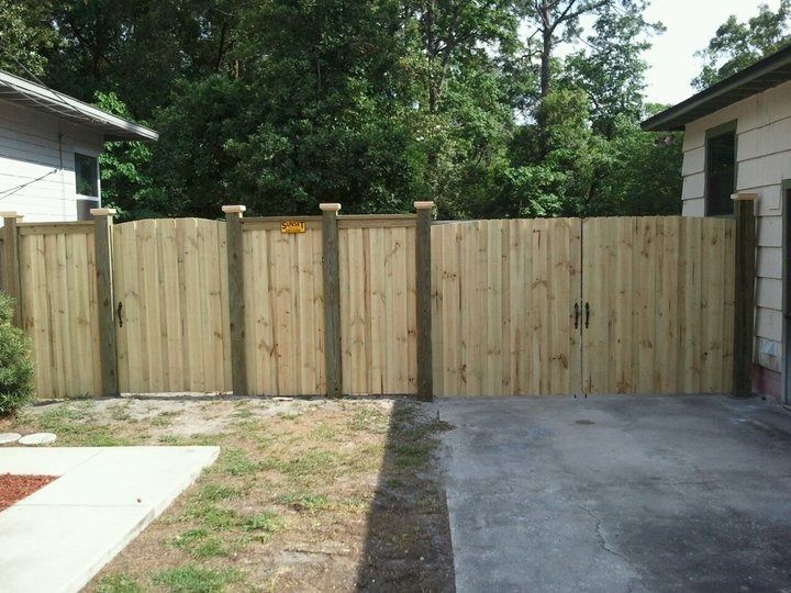 A wooden privacy fence with double gates installed across a residential driveway between two houses.