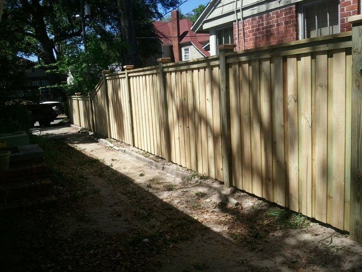 A newly installed wooden privacy fence runs alongside a dirt path next to a residential home.