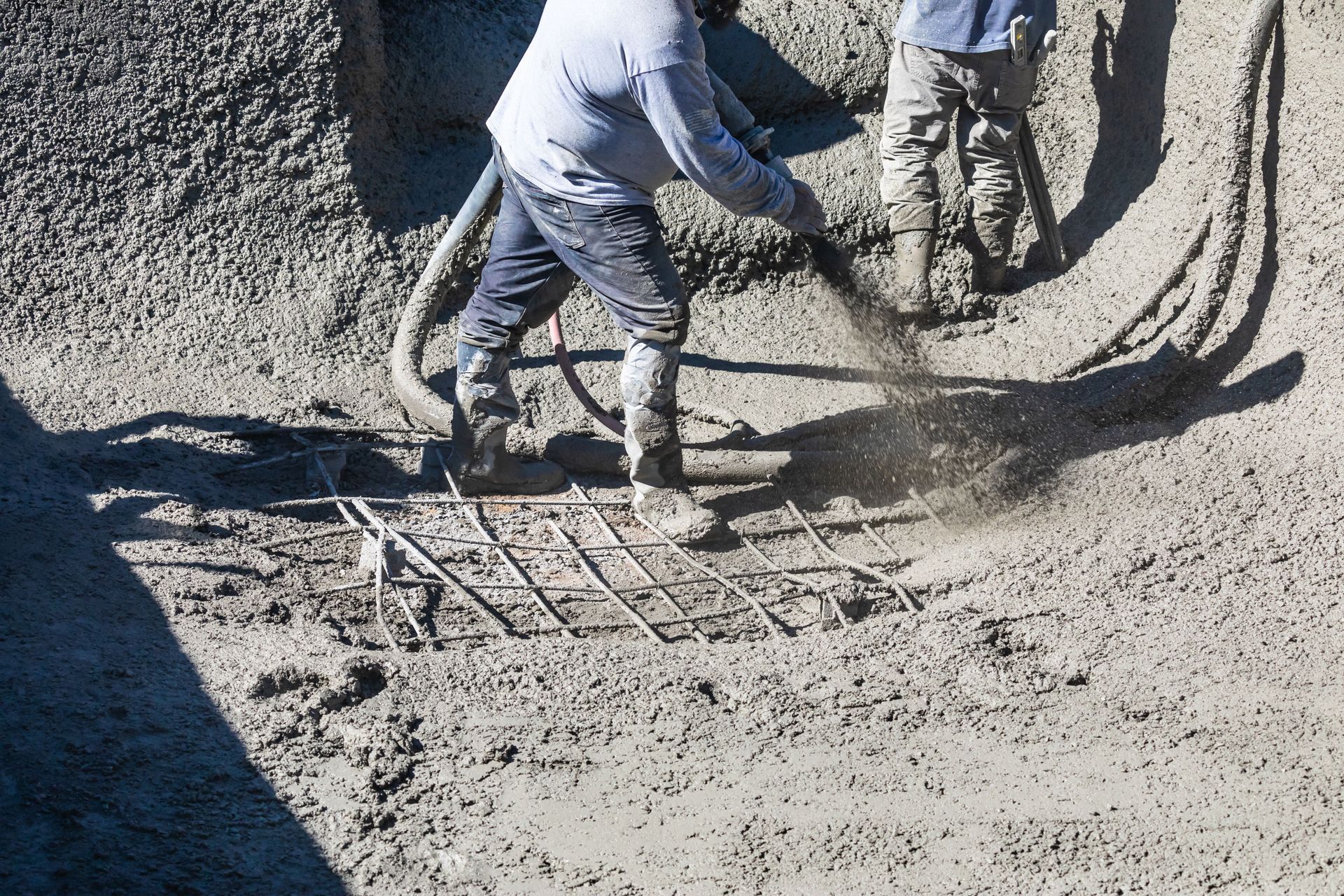 Workers in blue gear smoothing wet concrete with tools in a construction area