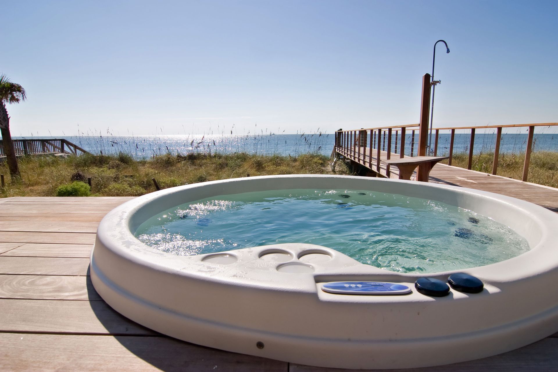 Round hot tub on a wooden deck overlooking the ocean under a clear blue sky