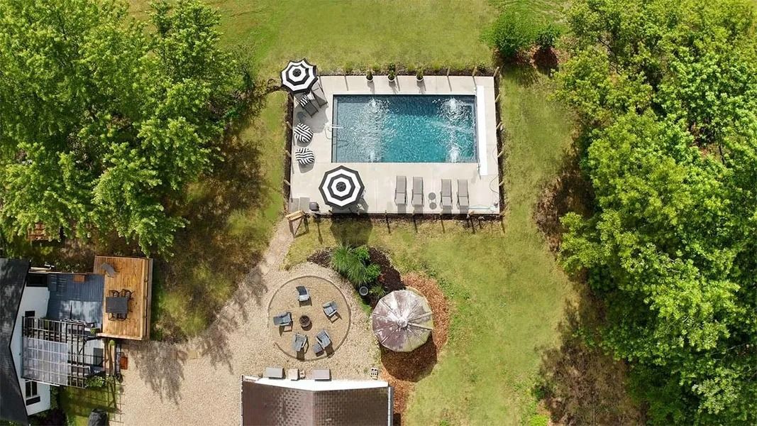 Aerial view of a backyard with a rectangular swimming pool, patio area, and surrounding trees.