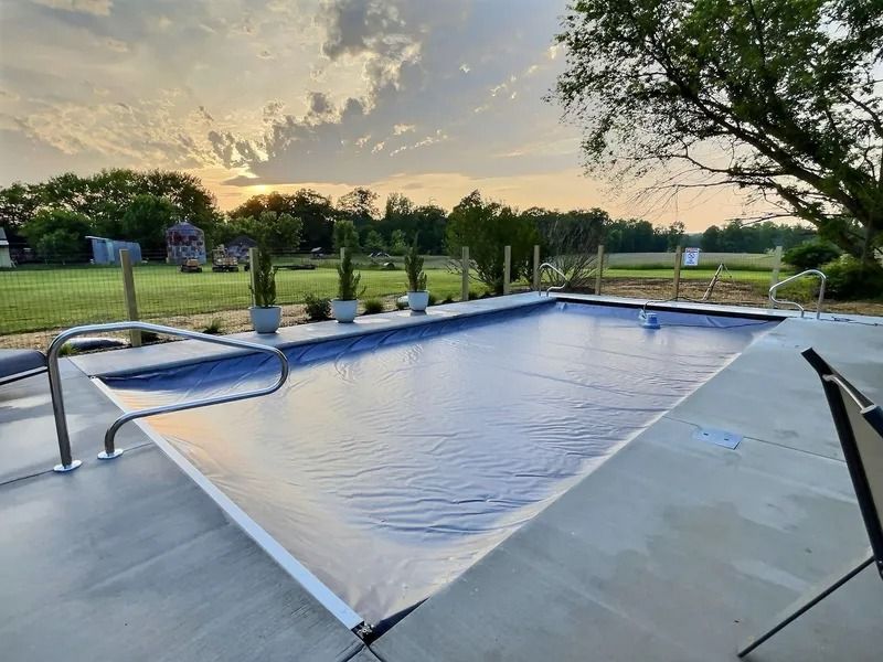 Empty covered pool with metal handrails at sunset, beside a grassy lawn and trees