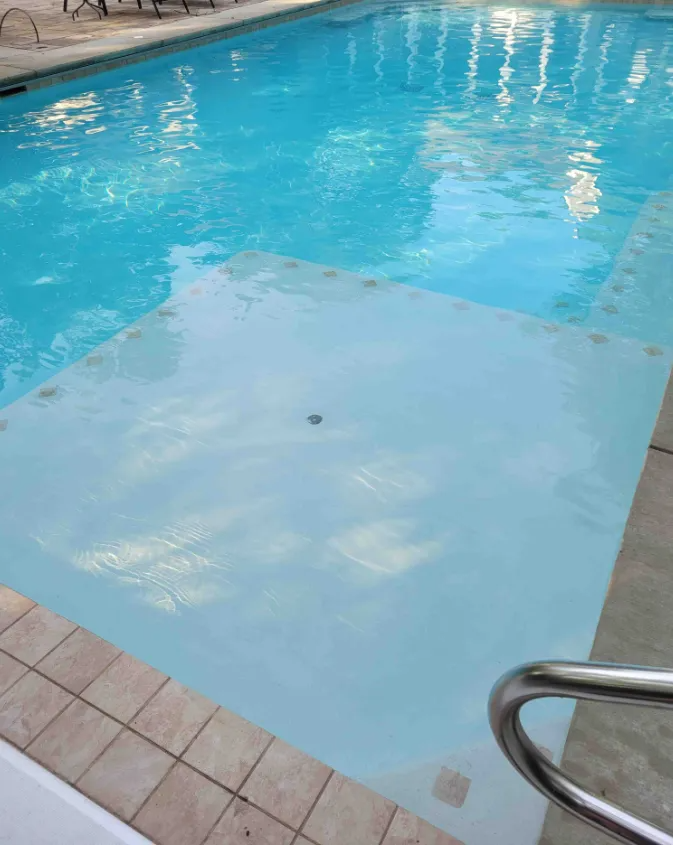 Accessible pool ramp with white non-slip surface leading into blue water
