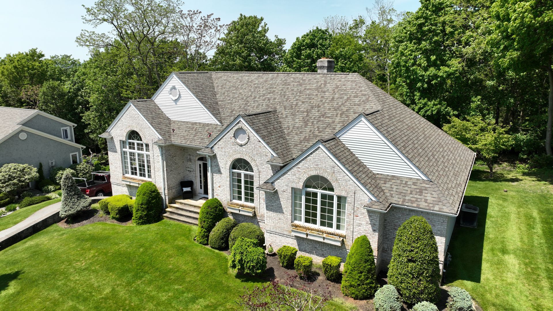An aerial view of a large house with a lush green lawn and trees in the background.