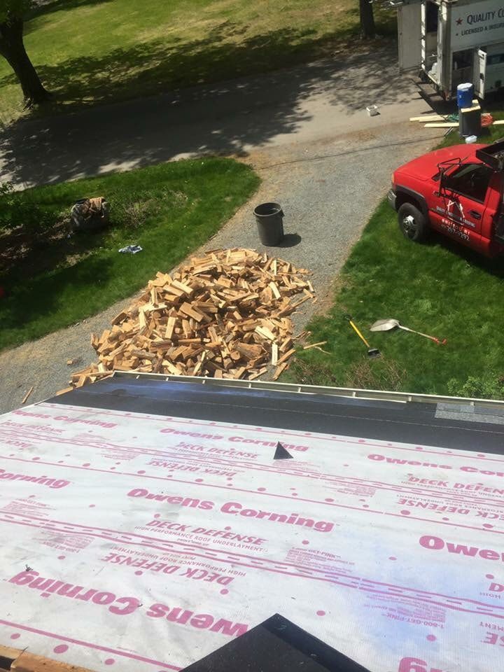 A red truck is parked in a driveway next to a pile of wood.