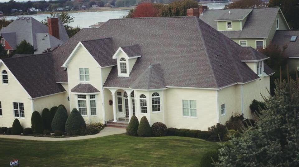 A large white house with a gray roof is surrounded by other houses