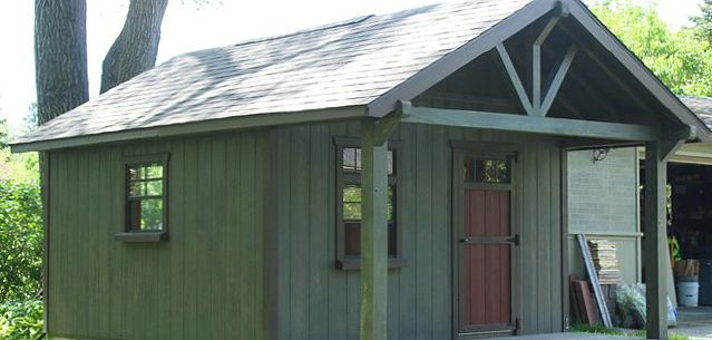 A small shed with a porch and a window is sitting next to a garage.