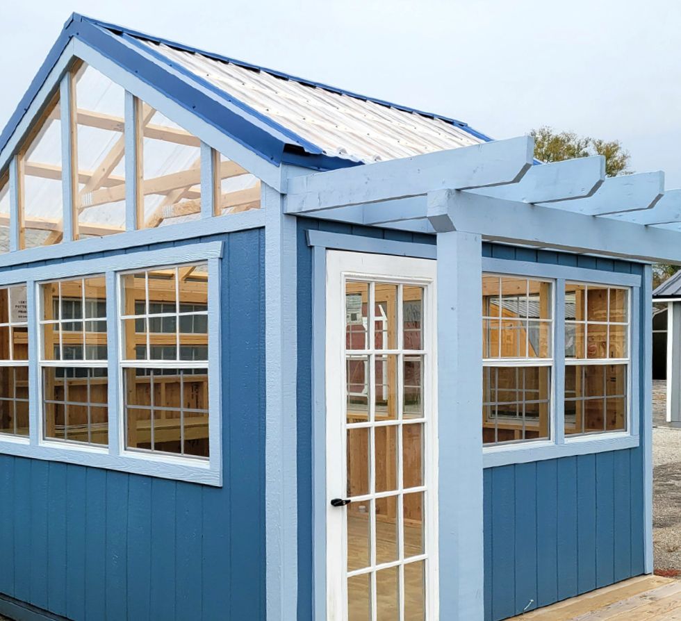 A blue shed with a white door and lots of windows
