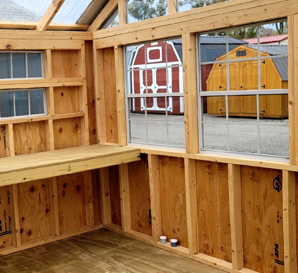 A wooden shed with a red barn in the background