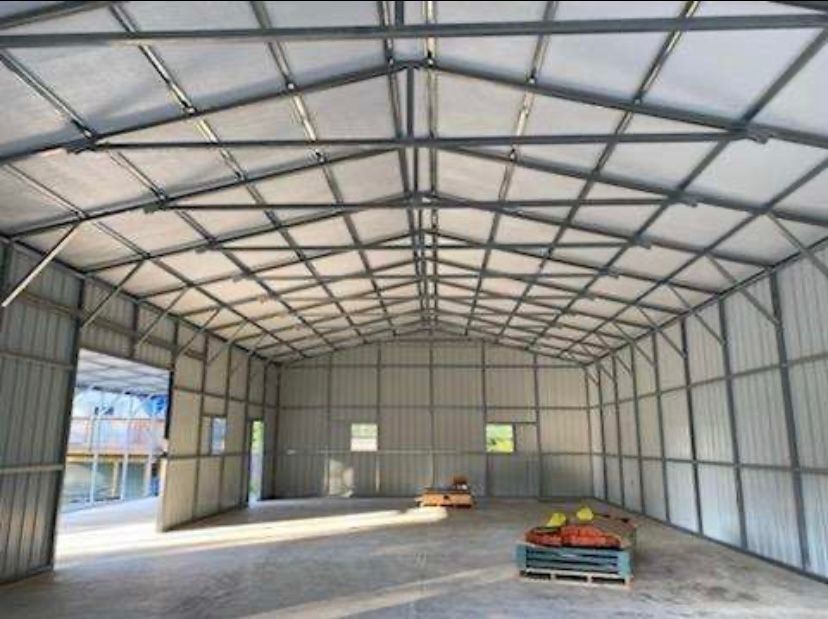 Inside view of a metal framed warehouse with gray walls and ceiling, empty. Three pallets with items sit on the floor.