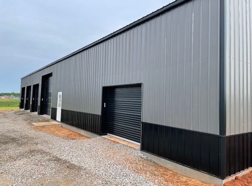 A long, gray metal building with black accents and multiple garage doors on a gravel lot.