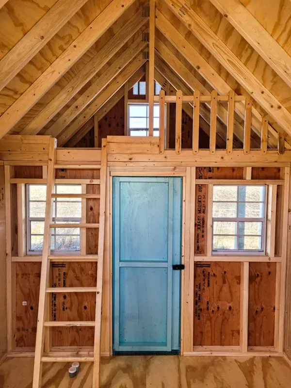 A wooden room with a blue door and a ladder