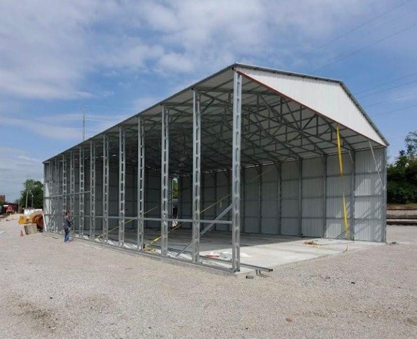 Partially constructed metal building on a gravel lot, under a blue sky.