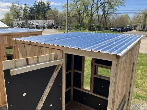 A wooden shed with a metal roof is sitting in the grass.