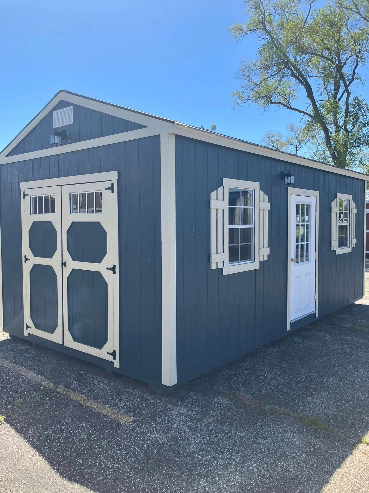 A gray shed with white doors and windows is sitting on top of a gravel lot.