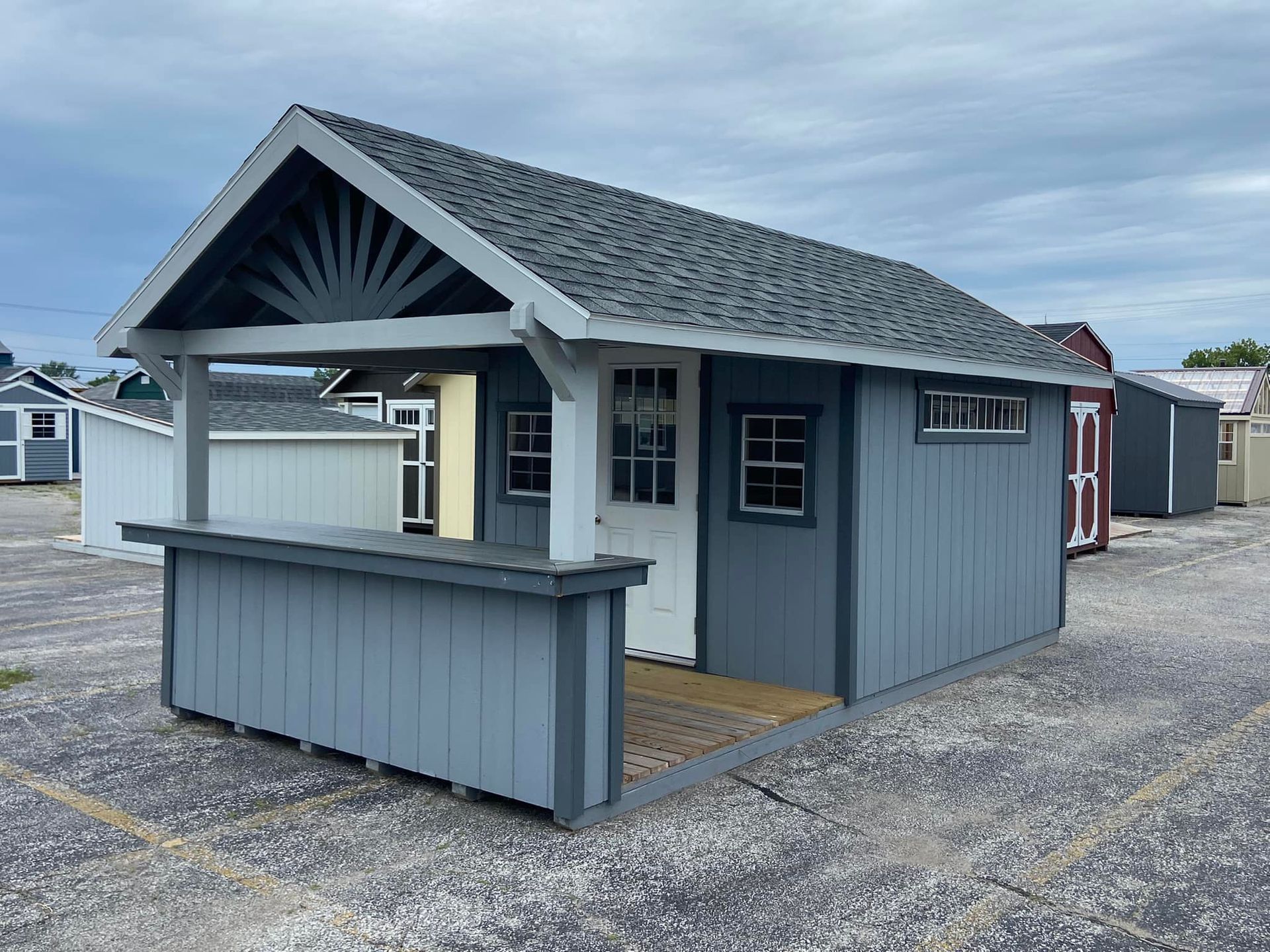 A small shed with a porch and a roof is sitting on top of a gravel lot.