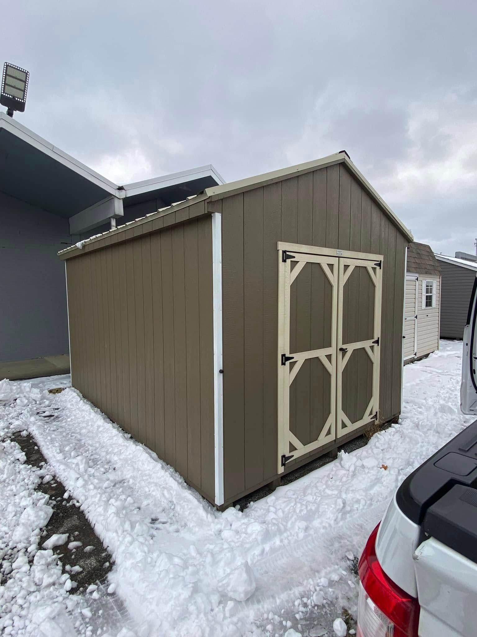 A shed is sitting in the snow next to a truck.