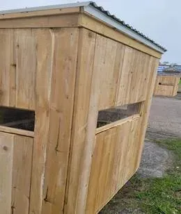 A wooden shed with a metal roof is sitting in the grass.