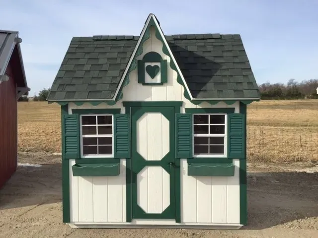 A white and green playhouse with a heart on the roof