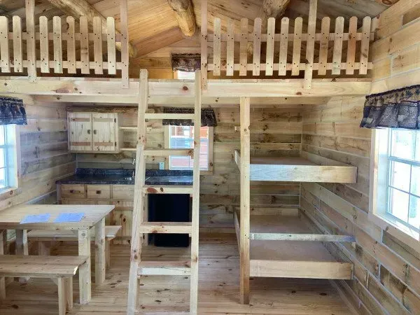 The inside of a log cabin with bunk beds and a ladder.