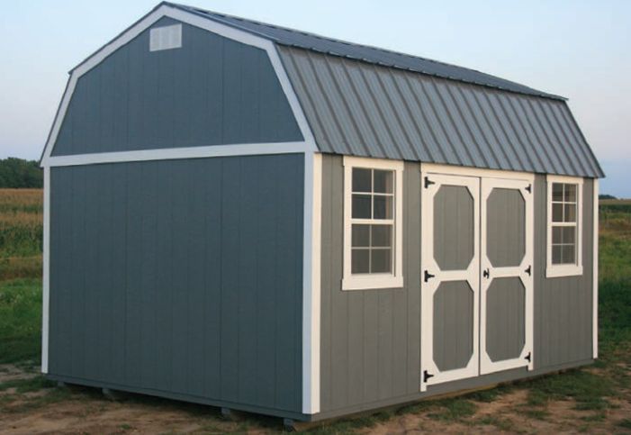 A barn shed with a metal roof is sitting in the middle of a field.