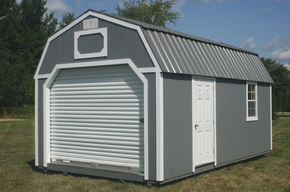 A gray and white barn with a garage door is sitting in the middle of a grassy field.