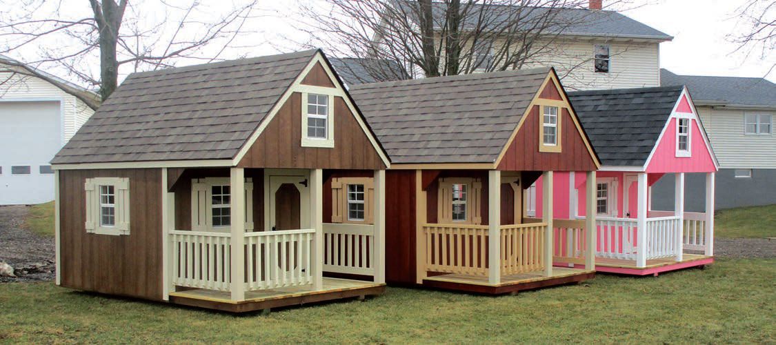 A row of playhouses are lined up in a grassy field.