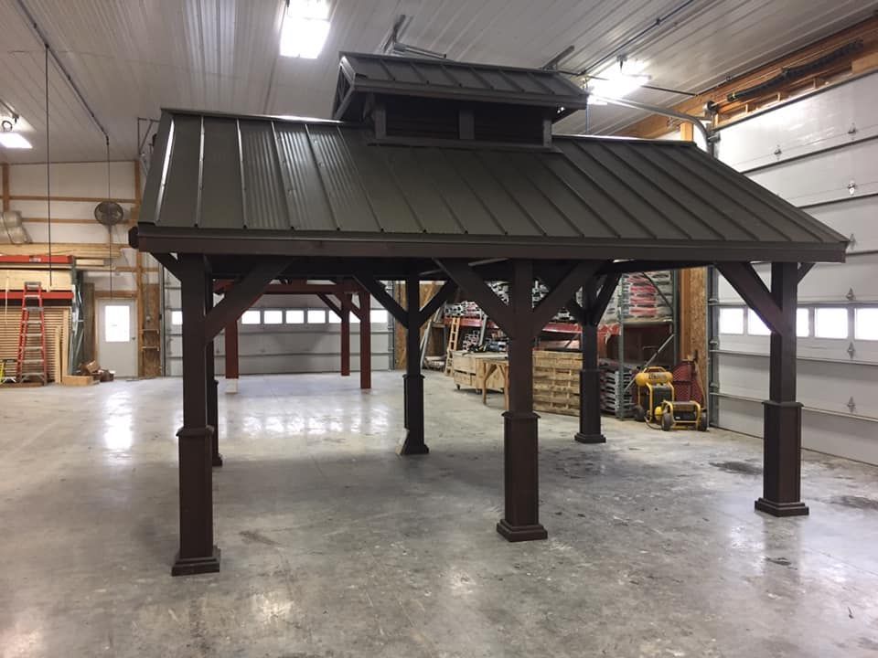 A large wooden gazebo with a metal roof is sitting in a warehouse.
