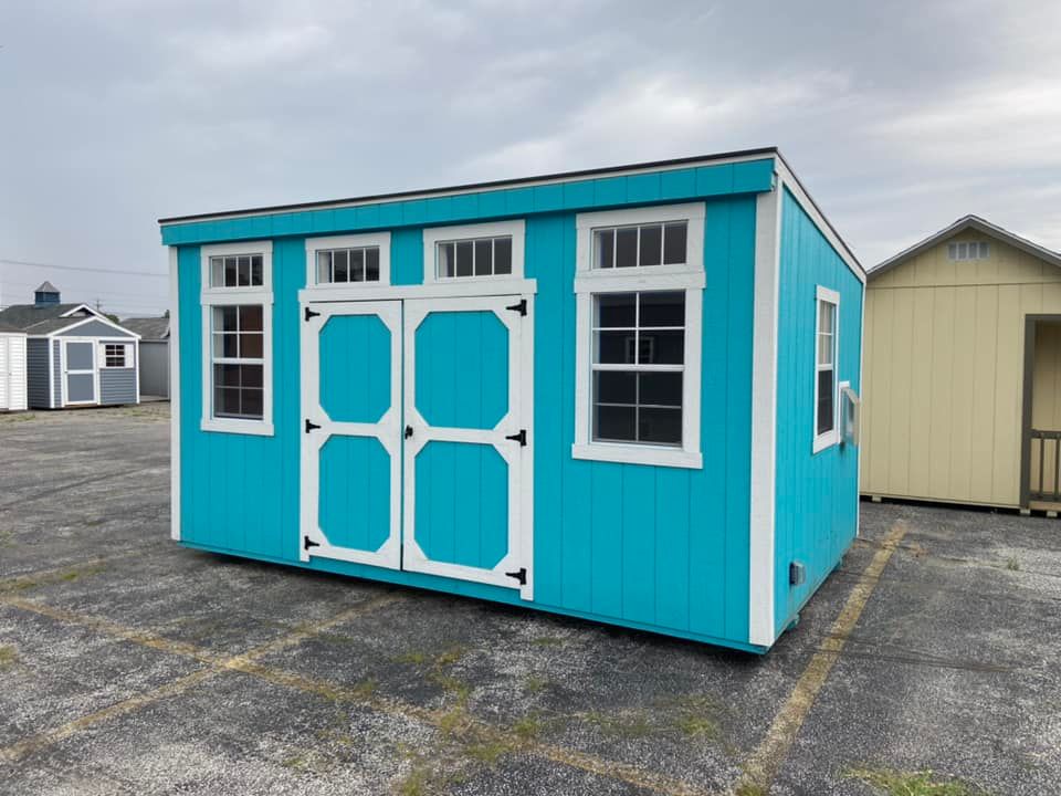 A blue shed with white trim is sitting in a parking lot.