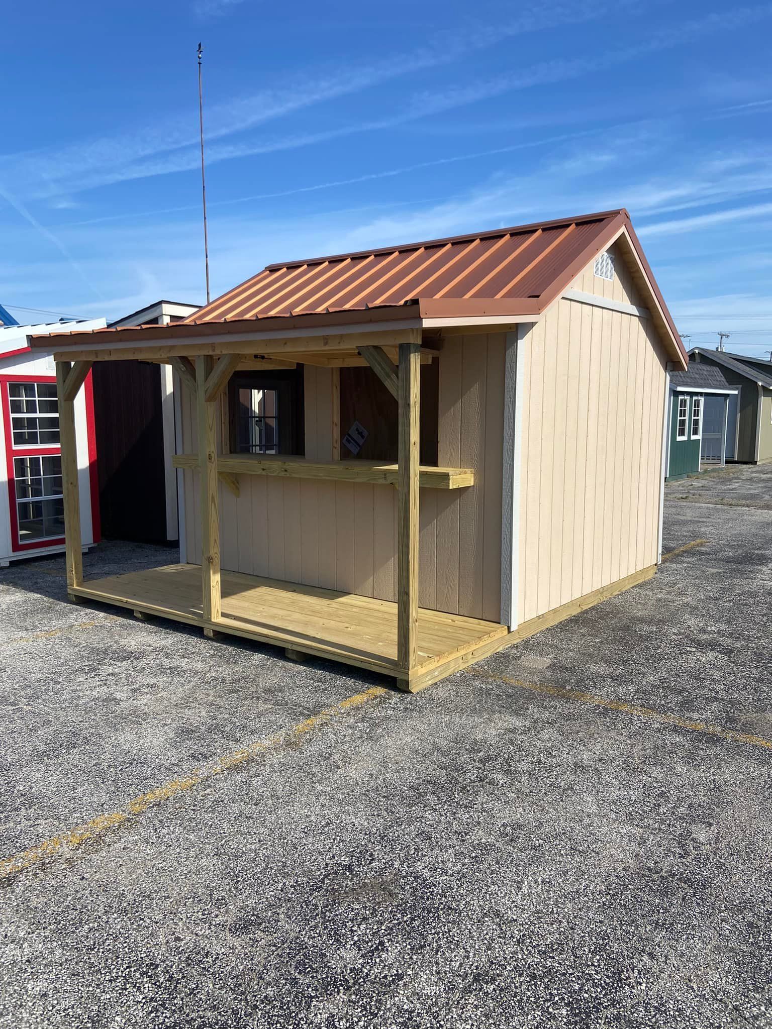 A small shed with a porch and a copper roof is sitting on top of a gravel lot.