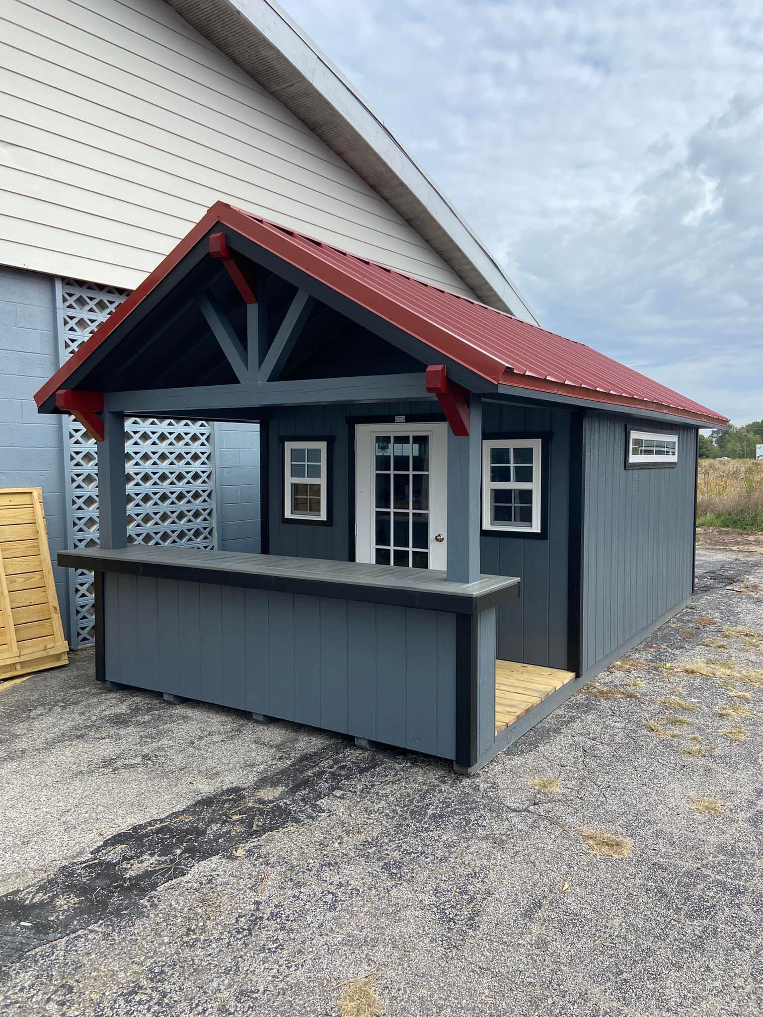 A small shed with a red roof and a counter in front of a building.