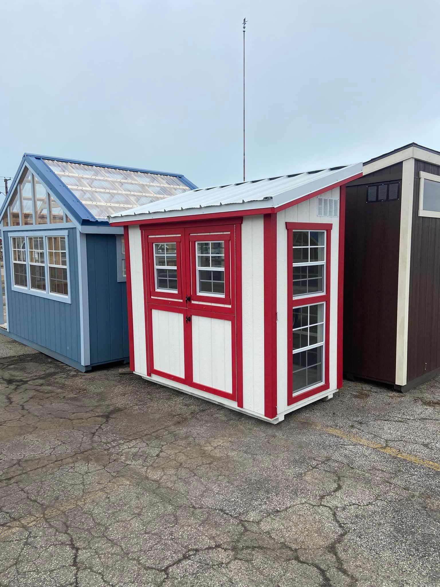 A red and white shed is sitting next to a blue shed and a brown shed.
