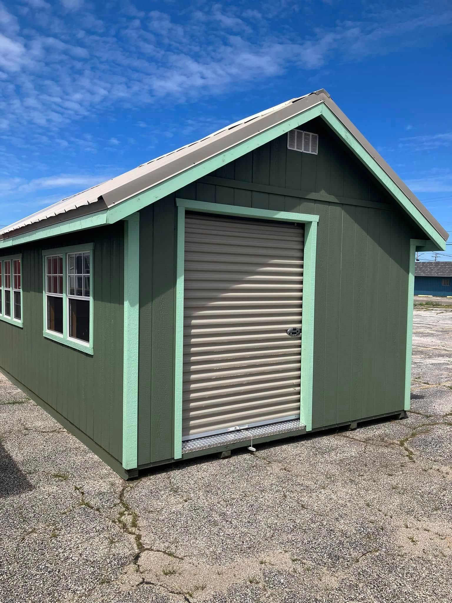 A green shed with a garage door is sitting on top of a gravel lot.